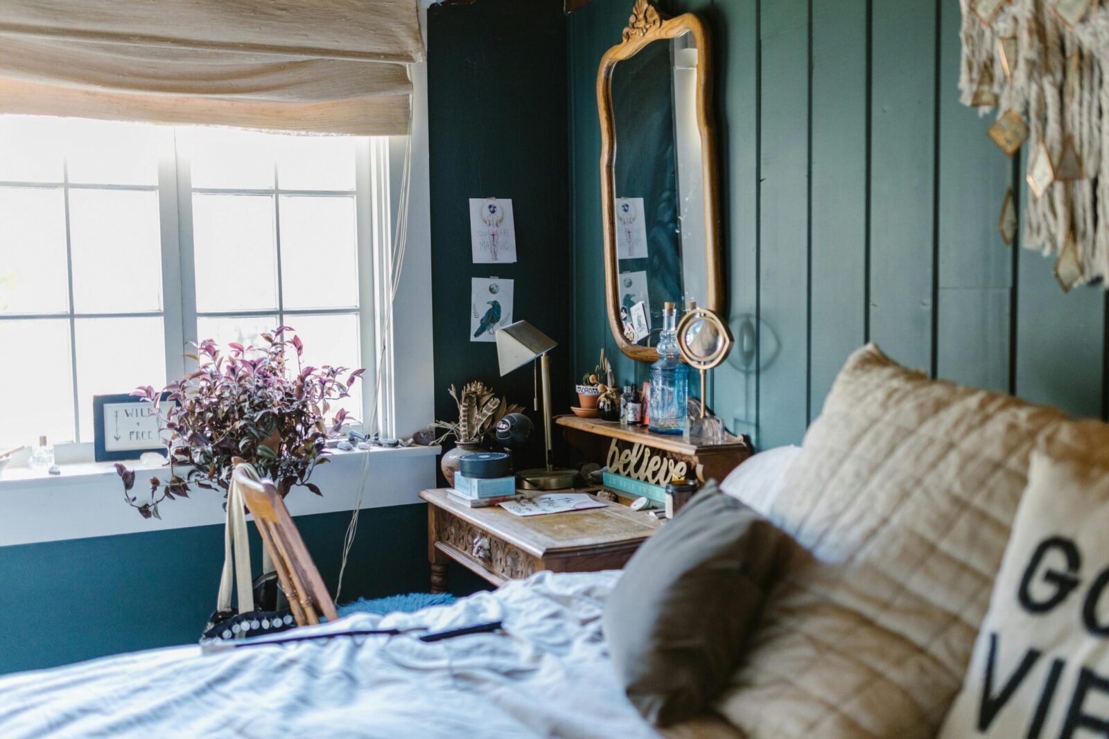 A cozy bedroom with green walls featuring crystals and a vintage mirror.